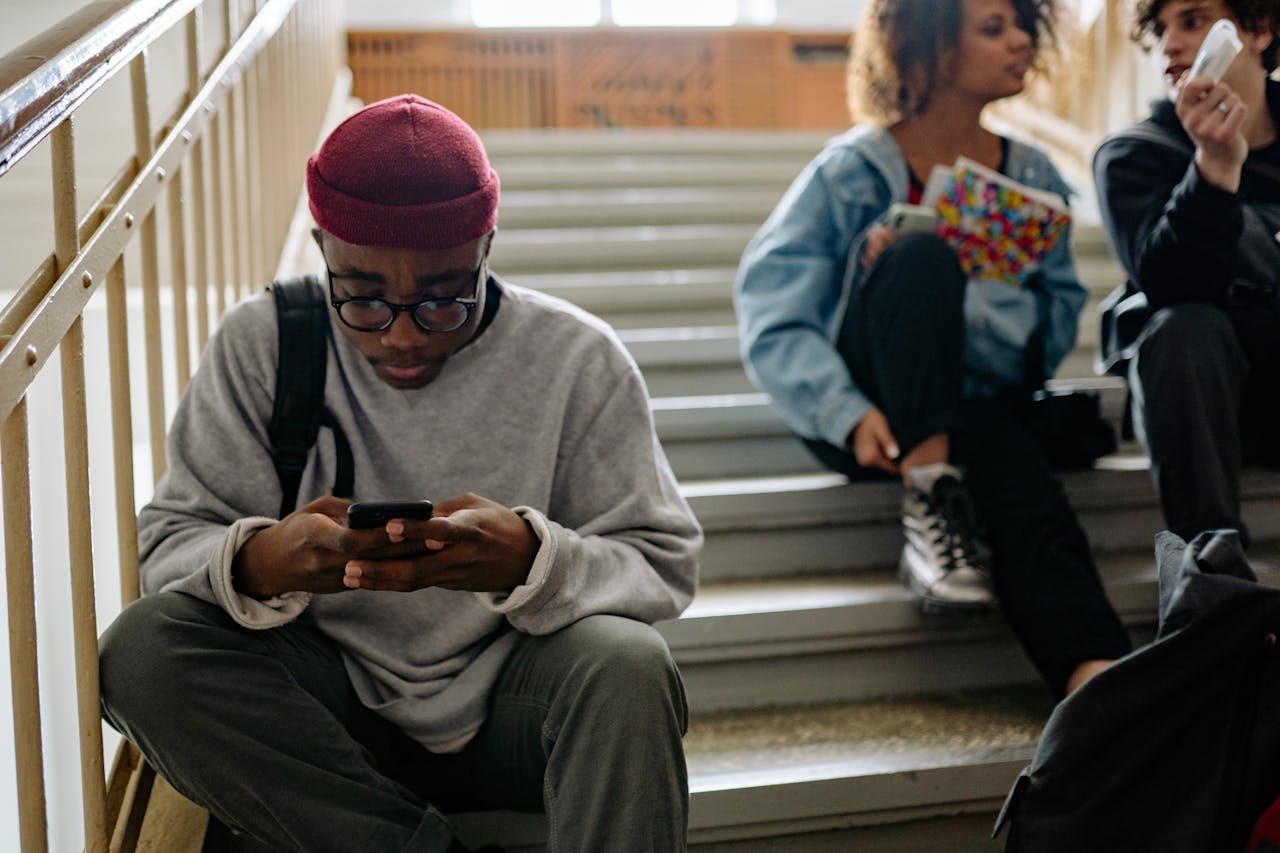 Photo of a young black man reading his phone on the steps.